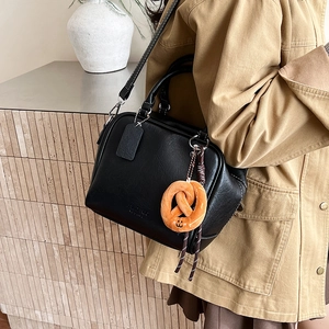Detail einer schwarzen Bowling-Tasche aus Kieselleder mit süßem Brezel-Plüsch-Anhänger