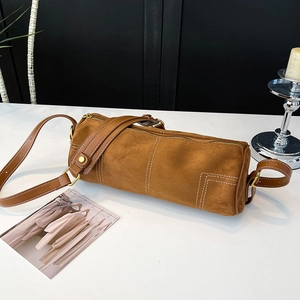 Detail of brown cylinder bag with contrast white stitching and long leather strap