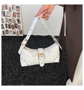 Détail d'un sac à main en cuir verni blanc avec boucles dorées et rivets décoratifs