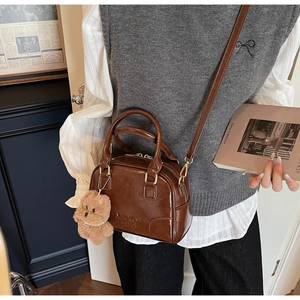 Detail of dark brown pillow bag with MKXQ logo, glossy leather and bear charm decoration