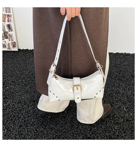 Gros plan d'un sac sous le bras en cuir verni blanc avec clous et boucles dorés