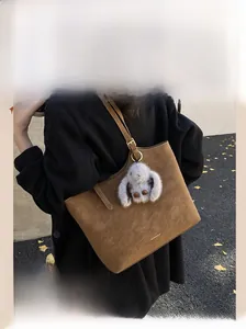 Brown suede tote bag with plush rabbit pendant shown in an outdoor street style shot