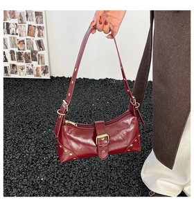 Détail d'un sac sous le bras bordeaux brillant avec rivets décoratifs et boucle dorée
