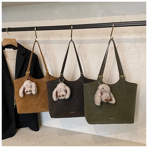 Three suede leather tote bags in brown, coffee, and green colors with plush rabbit charms