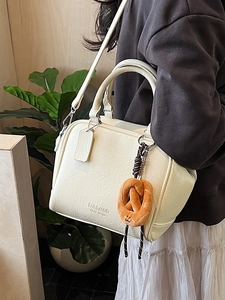 Cremeweiße Boston-Tasche mit Lederstruktur und Brezel-Anhänger an einem Modell