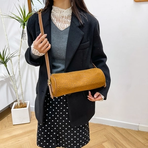 Brown grainy leather cylinder bag with adjustable strap worn by model in a minimalist setting