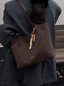 Brown leopard print tote bag with beaded tassel shown on a shoulder in a stylish outdoor setting