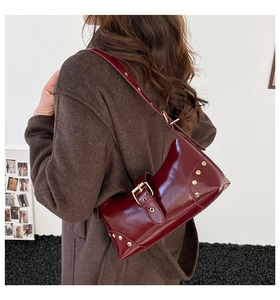 Détail du sac bandoulière rouge brillant avec boucles dorées et rivets décoratifs