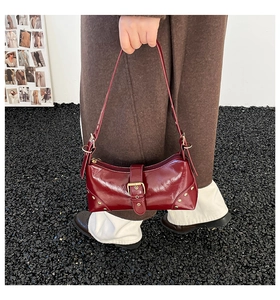 Gros plan du sac à bandoulière rouge foncé brillant avec clous dorés et sangle à boucle