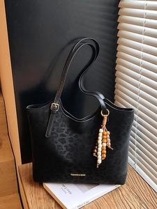 Black leopard print tote bag with adjustable strap and bohemian tassel on wood surface
