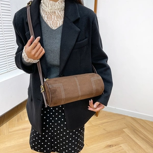 Detail of dark brown cylinder bag with suede texture and contrast white stitching