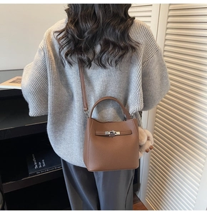 Borsa a secchiello in pelle marrone con chiusura rotante argento e tracolla in un set di interni