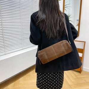 Detail of retro brown cylinder shoulder bag featuring white contrast stitching accents