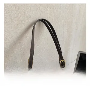 Detail of adjustable shoulder strap with gold buckle and fuzzy charm on brown tote bag