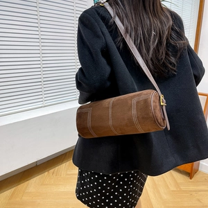 Detail view of brown matte cylinder bag with contrast white stitching and gold buckle