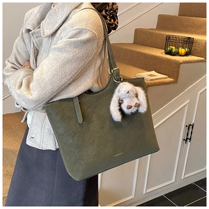 Detail of olive green tote bag featuring a gold logo and a plush rabbit charm accessory