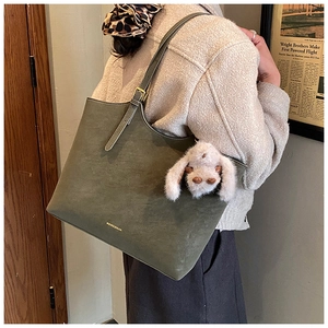 Detail of olive green suede tote bag featuring adjustable strap and plush bunny charm