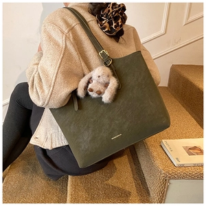 Detail of dark green suede tote bag with plush rabbit pendant and metallic gold buckle