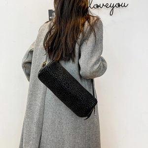 Close-up of black leopard print cylinder bag with matte finish and golden buckle details