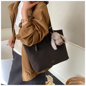 Detail of dark brown tote bag in matte texture with a cute plush rabbit charm accessory