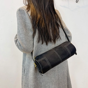 Close-up of black cylinder shoulder bag with white contrast stitching and gold zipper