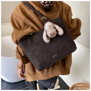 Detail of dark brown leather tote bag with plush rabbit charm and gold logo lettering