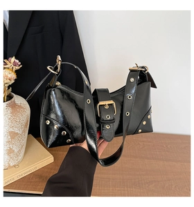 Détails d'un sac porté épaule en cuir verni noir brillant avec rivets et œillets dorés