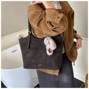 Detail of dark brown tote bag with gold brand logo and plush charm accessory