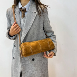 Detail of brown suede cylinder shoulder bag with contrasting white stitching and metal buckle
