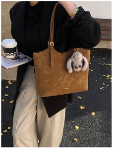 Brown faux leather tote bag with plush rabbit charm and embossed letters in outdoor setting