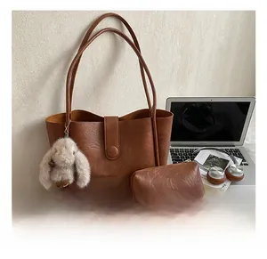Vintage brown leather tote bag with matching pouch and plush rabbit charm in a desk setting