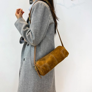 Detail of tan barrel bag with white contrast stitching and gold-tone hardware on model