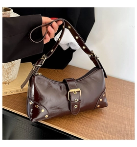 Détail d'un sac à bandoulière en cuir verni bordeaux avec des clous dorés et une boucle