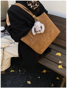 Close-up of brown suede tote bag with plush rabbit pendant and metallic adjustable buckle