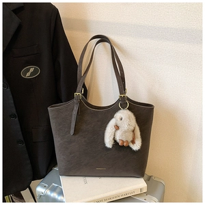 Detail of dark brown leather tote bag on luggage with plush rabbit charm and gold hardware
