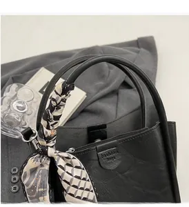Vue détaillée d'un sac à main noir en cuir avec foulard en soie sur un blazer gris