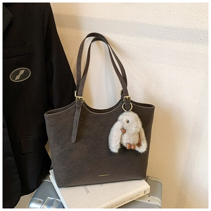 Detail of a large brown leather tote bag with gold hardware and a plush bunny charm