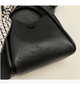 Détail du sac seau en cuir noir avec texture plissée et foulard en soie sur la poignée
