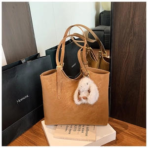 Brown tote bag detail with long shoulder strap and fluffy white rabbit charm accessory