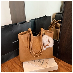 Detailed texture of brown leather tote bag with white bunny plush charm on a table