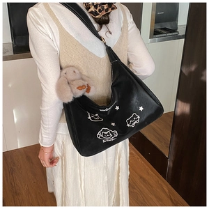 Detalle de bolso hobo negro con bordado de gato blanco y colgante de conejo de peluche