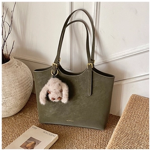 Olive green tote bag with plush rabbit charm and gold buckles on a warm indoor setting