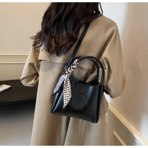 Modern black leather bucket bag styled with a patterned silk scarf on a trench coat