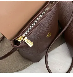 Detailed close-up of dark brown litchi grain leather bag with smooth golden zipper
