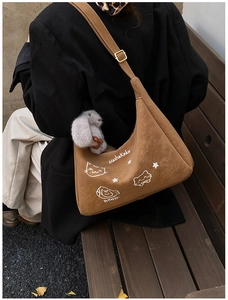 Detalle de un bolso hobo de gamuza marrón con bordado de gato y colgante de conejo