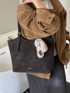 Deep brown matte leather tote bag with adjustable straps and plush charm accessory