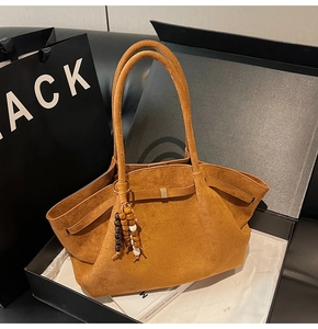 Detail of brown suede tote bag featuring contrast bead tassel charm and textured finish