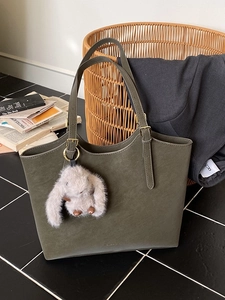 Olive green faux leather tote bag with plush bunny charm on black tiled background