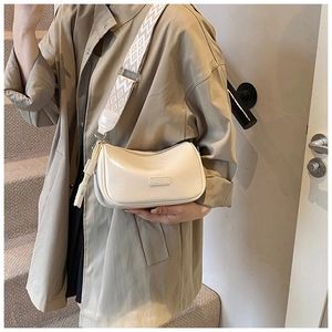 Detail of cream pillow bag showing wide patterned strap and polished metal logo plate