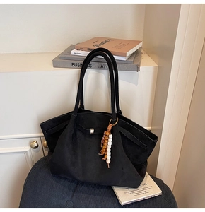 Detail of black suede tote bag with metal buckle and wooden bead charm on a soft chair